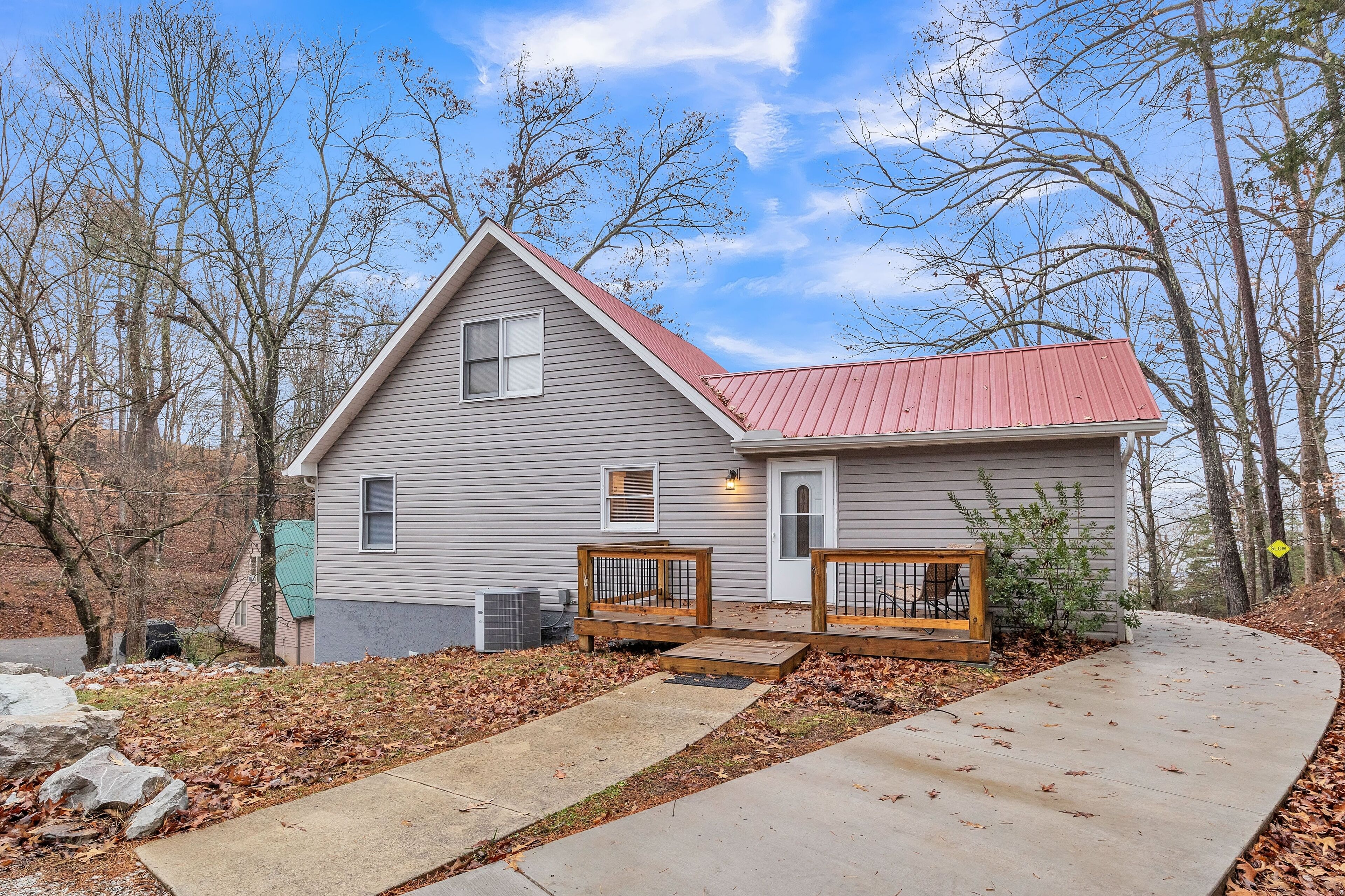 A two-story house with a red roof, a front porch with wooden benches, and a concrete driveway.