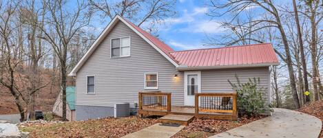 A two-story house with a red roof, a front porch with wooden benches, and a concrete driveway.