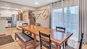 A modern kitchen with white cabinets, a stainless steel refrigerator, and a wooden dining table with chairs. - Deerfield Hideaway At Old Smokey 5 Bedroom Home (La Follette)