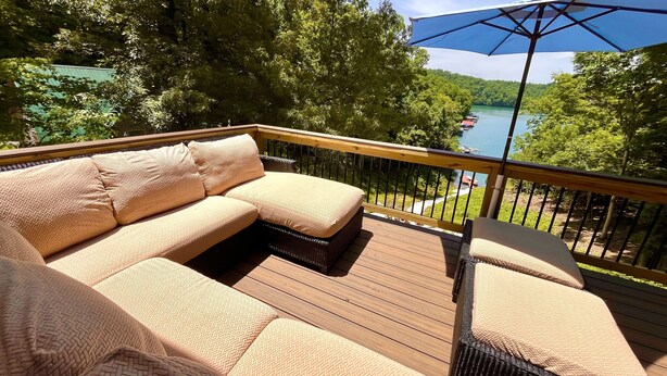A wooden deck with a beige sectional sofa and a wicker chair, overlooking a lake with boats. - Deerfield Hideaway At Old Smokey 5 Bedroom Home (La Follette)