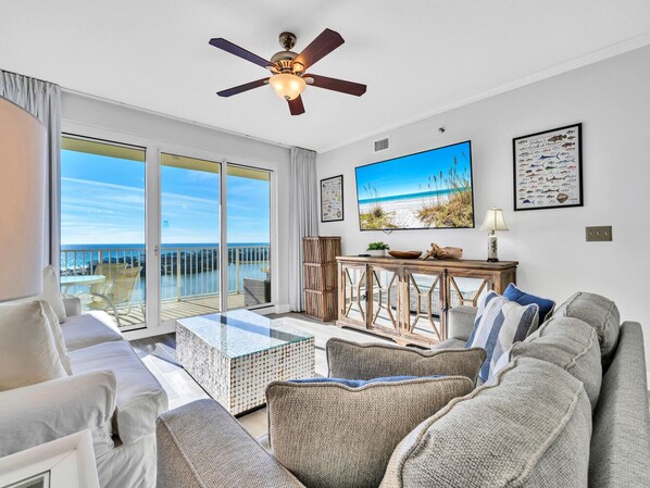 A spacious living room with a large window, a ceiling fan, and a view of the ocean.