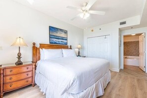 Ein Schlafzimmer mit einem großen Bett, einem Deckenventilator, einem Gemälde, einem Nachttisch und einer Tür zu einem Badezimmer.