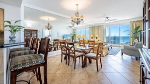 A spacious living area with a dining set, a chandelier, and a view of the ocean. - Spectacular view of the Gulf and just steps away from the pool and beach! (Miramar Beach)