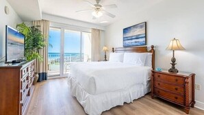 A hotel room with a large bed, a ceiling fan, a TV, a dresser, and a view of the ocean through the balcony doors. - Spectacular view of the Gulf and just steps away from the pool and beach! (Miramar Beach)