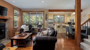 A spacious living room with a fireplace, leather sofa, wooden coffee table, and large windows. - L'Aiglon - Pool, Golf & Tremblant (Mont-Tremblant)