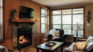 A cozy living room with a fireplace, leather furniture, and large windows. - L'Aiglon - Pool, Golf & Tremblant (Mont-Tremblant)
