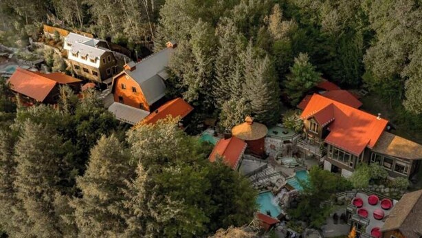 An aerial view of a resort with multiple buildings, a swimming pool, and a forested area. - L'Aiglon - Pool, Golf & Tremblant (Mont-Tremblant)
