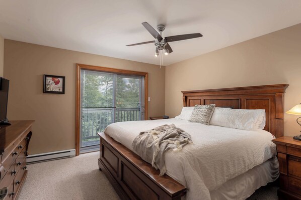 A bedroom with a bed, a ceiling fan, a dresser, a nightstand, and a window with blinds. - L'Aiglon - Pool, Golf & Tremblant (Mont-Tremblant)