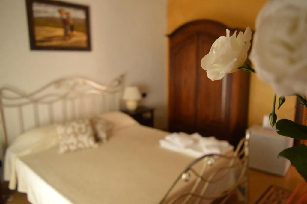 Ein ordentlich bezogenes Bett mit weißer Decke und Kissen, ein Holzschrank und eine weiße Blume in einer Vase.