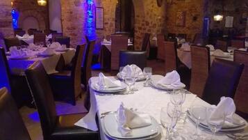 Un restaurant où les tables sont dressées pour le service, avec des murs en pierre et un éclairage chaleureux.