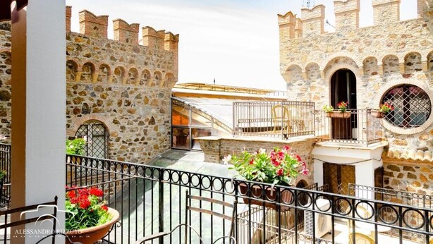 Un patio con paredes de piedra, un balcón con barandilla de metal y plantas en macetas.