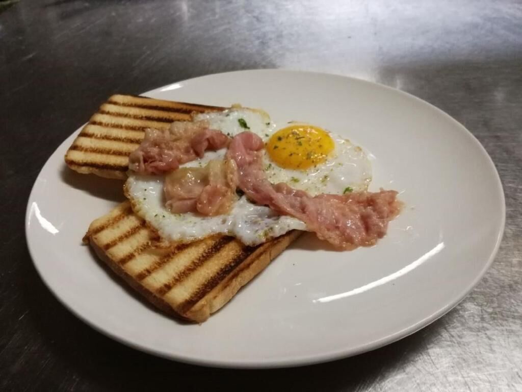 A plate with a grilled egg, bacon, and toast.