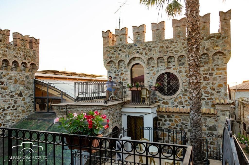 A stone building with a balcony, a palm tree, and a sign for "Alessandro Rizzuto."