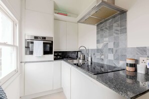Una cocina moderna con armarios blancos, horno de acero inoxidable, encimera de granito y salpicadero de azulejos.