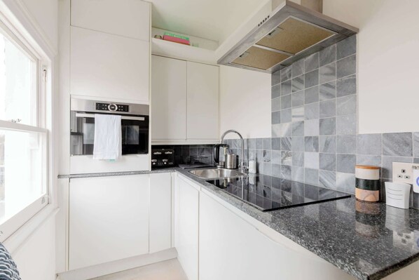 A modern kitchen with white cabinets, a stainless steel oven, a granite countertop, and a tiled backsplash.