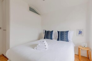 Ein ordentlich bezogenes Bett mit weißer Bettwäsche und einem Stapel weißer Handtücher.