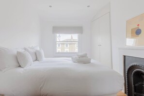 A white bedroom with a bed, a window, and a fireplace.