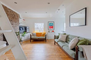 A modern living room with a sofa, a small table, a TV, and a brick wall.
