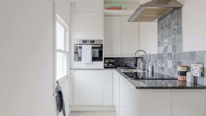 Een moderne keuken met witte kasten, een inbouwoven, een roestvrijstalen afzuigkap en een granieten aanrecht.