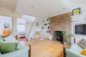 A modern living room with a fireplace, wooden flooring, and a staircase leading to another room.