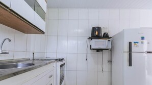 Une cuisine avec des murs recouverts de carreaux blancs, un évier en acier inoxydable, un four encastré, un réfrigérateur et une machine à café fixée au mur.