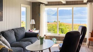A cozy living room with a grey sofa, a round table, and a view of a lake and mountains. - 4 Person Holiday Home in Alsvag (Oksnes)