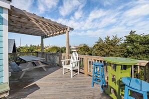 Une terrasse en bois agrémentée d’une pergola, d’une chaise Adirondack blanche et de deux tabourets de bar bleus.
