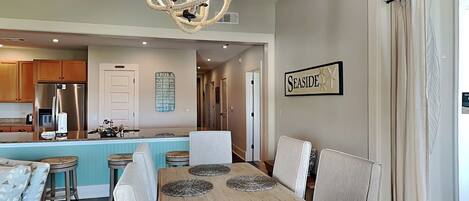 A modern kitchen with stainless steel appliances, a central island with bar stools, and a dining area with a wooden table and woven placemats.