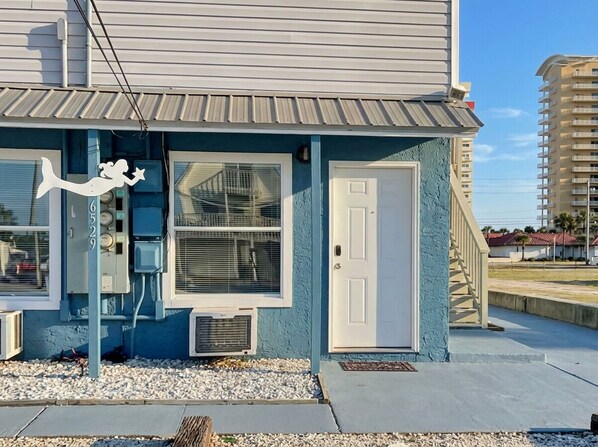 Un bâtiment à l’extérieur bleu, avec une porte blanche et un petit porche.