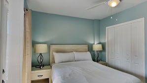 Una cama bien hecha en una habitación con paredes color turquesa, un cabecero de madera, dos mesitas de noche con lámparas y un ventilador de techo.