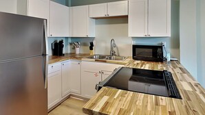 Una cocina moderna con armarios blancos, un refrigerador de acero inoxidable, un microondas negro y una encimera de madera.