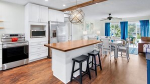A modern kitchen with white cabinets, stainless steel appliances, and a wooden island with stools. - Lido Beach Retreat - Book your romantic escape today! (Lido Key)