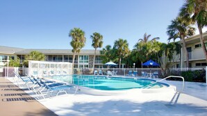 A pool area with lounge chairs, palm trees, and a building with balconies. - Lido Beach Retreat - Book your romantic escape today! (Lido Key)