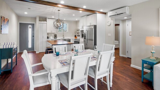A modern kitchen with white cabinetry, a central island, and a dining area with white chairs and a table. - Lido Beach Retreat - Book your romantic escape today! (Lido Key)