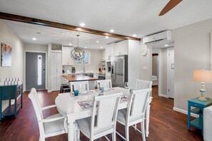 A modern kitchen with white cabinetry, a central island, and a dining area with white chairs and a table.