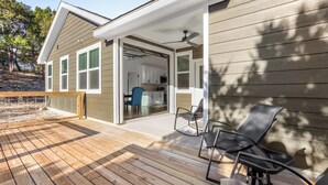 Una terraza de madera con mobiliario exterior, un porche cubierto y vistas al interior de la casa.