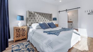 Un dormitorio con cama, mesitas de noche, ventilador de techo y vistas al baño.
