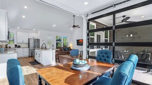 Una cocina moderna con armarios blancos, un refrigerador de acero inoxidable y un comedor con una mesa de madera y sillas azules.