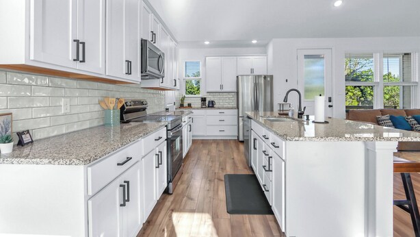 Una cocina moderna con gabinetes blancos, encimeras de granito y electrodomésticos de acero inoxidable, además de una isla central.