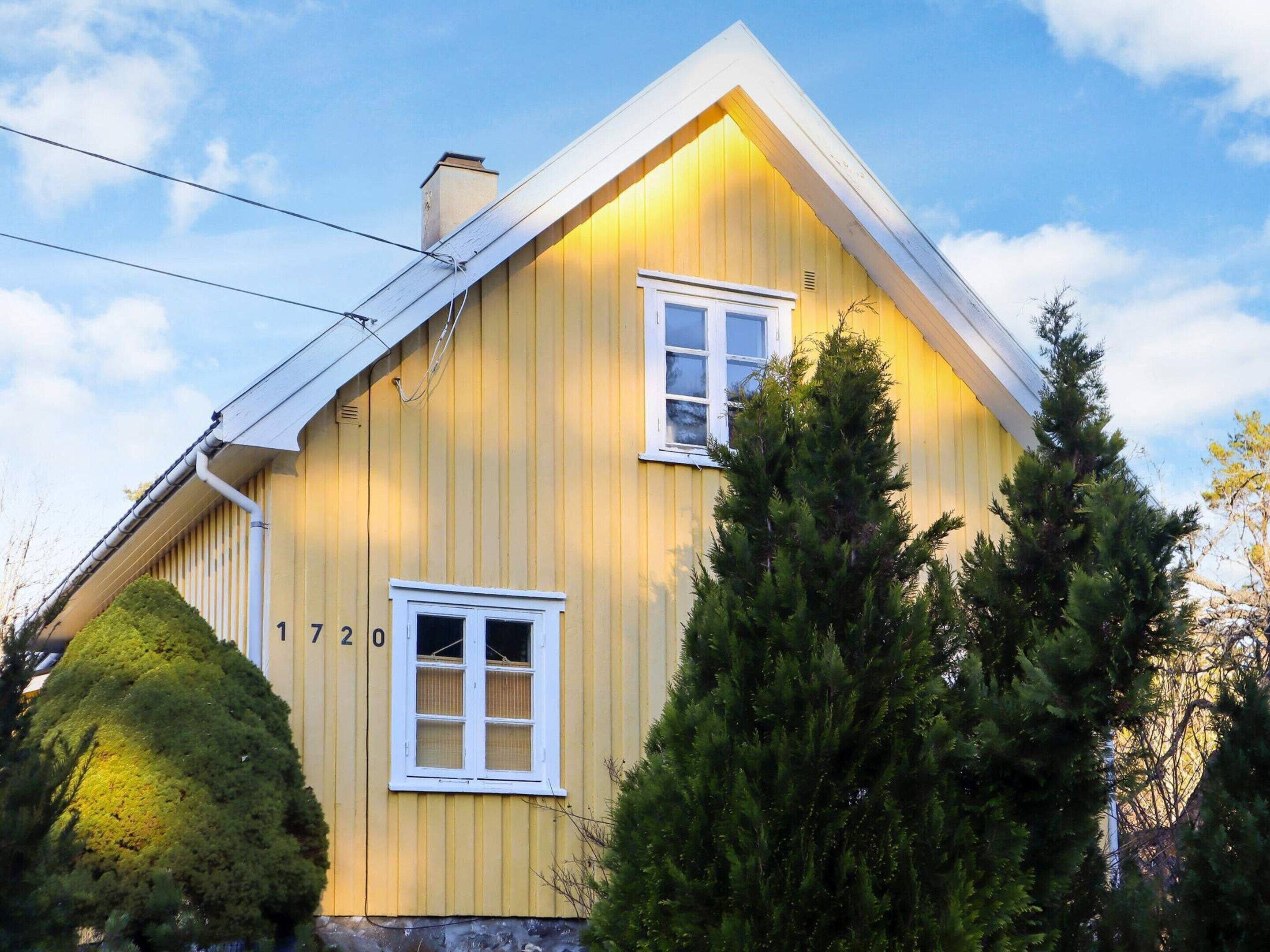 A yellow house with two windows and a chimney.