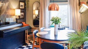 A modern dining area with a checkered floor, a round table, and chairs. There is a large mirror on the wall, a hanging pendant light, and a window with curtains. - 6 Person Holiday Home in Sondeled (Risør)