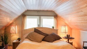 A cozy attic bedroom with a wooden sloped ceiling, a large bed with pillows, two hanging lamps, and a small table with candles. - 6 Person Holiday Home in Sondeled (Risør)