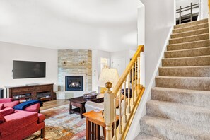 Un salon avec une cheminée, un escalier et un téléviseur à écran plat.