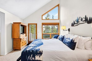 Ein Schlafzimmer mit einem großen Bett, einer Holzkommode, einem Fenster mit Blick auf Bäume und einer Wandlampe.