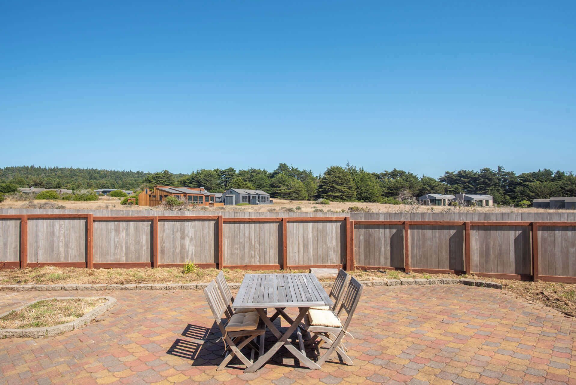A patio with a wooden table and chairs, surrounded by a wooden fence.