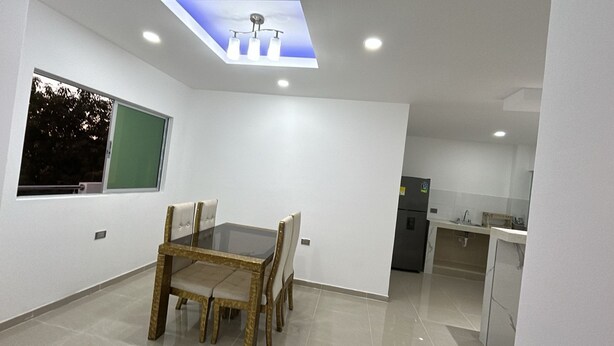Una cocina moderna con refrigerador empotrado, un comedor con mesa de vidrio y sillas acolchadas, y un techo con tragaluces.