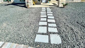 Um edifício de pedra com entrada coberta, um caminho de cascalho e um caminho de pedras que levam à entrada.