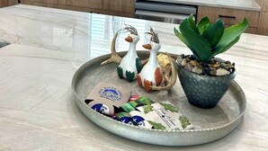 Uma cozinha com bancada de mármore, um letreiro com a mensagem 'Bem-vindo a Casa' e objetos decorativos, incluindo dois patos de cerâmica e uma planta em vaso.