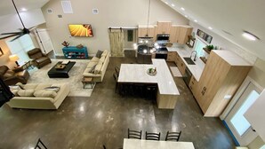 Ampla sala de estar com pé direito alto, mesa de jantar e cozinha equipada com eletrodomésticos modernos.