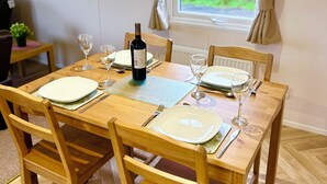 Une salle à manger avec une table en bois dressée pour quatre personnes, une bouteille de vin et une fenêtre avec des rideaux.